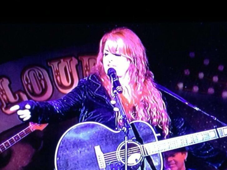 Wynonna Judd playing a guitar and singing on a live stage