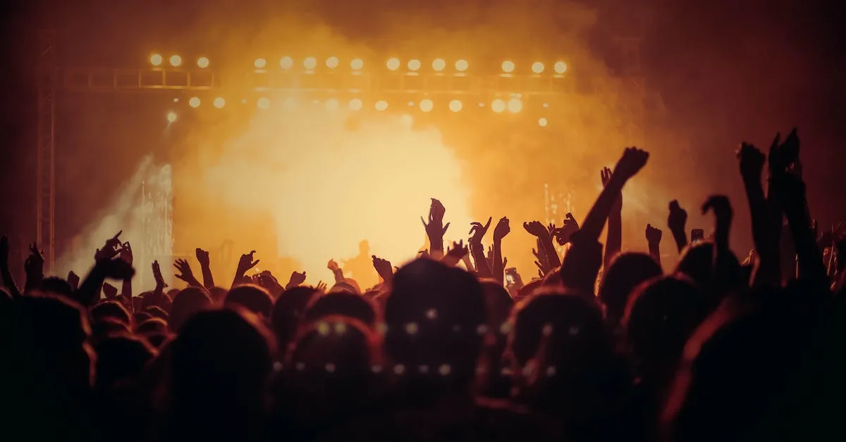 A photo of a large crowd of people at a concert, cheering and holding their phones up.