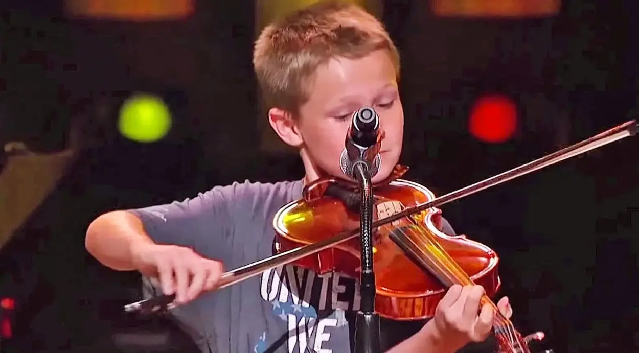 An image capturing Carson Peters on stage with his fiddle, showcasing his youthful energy and musical talent at the prestigious Grand Ole Opry.

