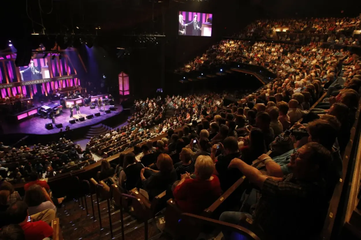 An image showing the enthralled audience at the Grand Ole Opry, applauding Carson Peters and Ricky Skaggs after their captivating performance of 