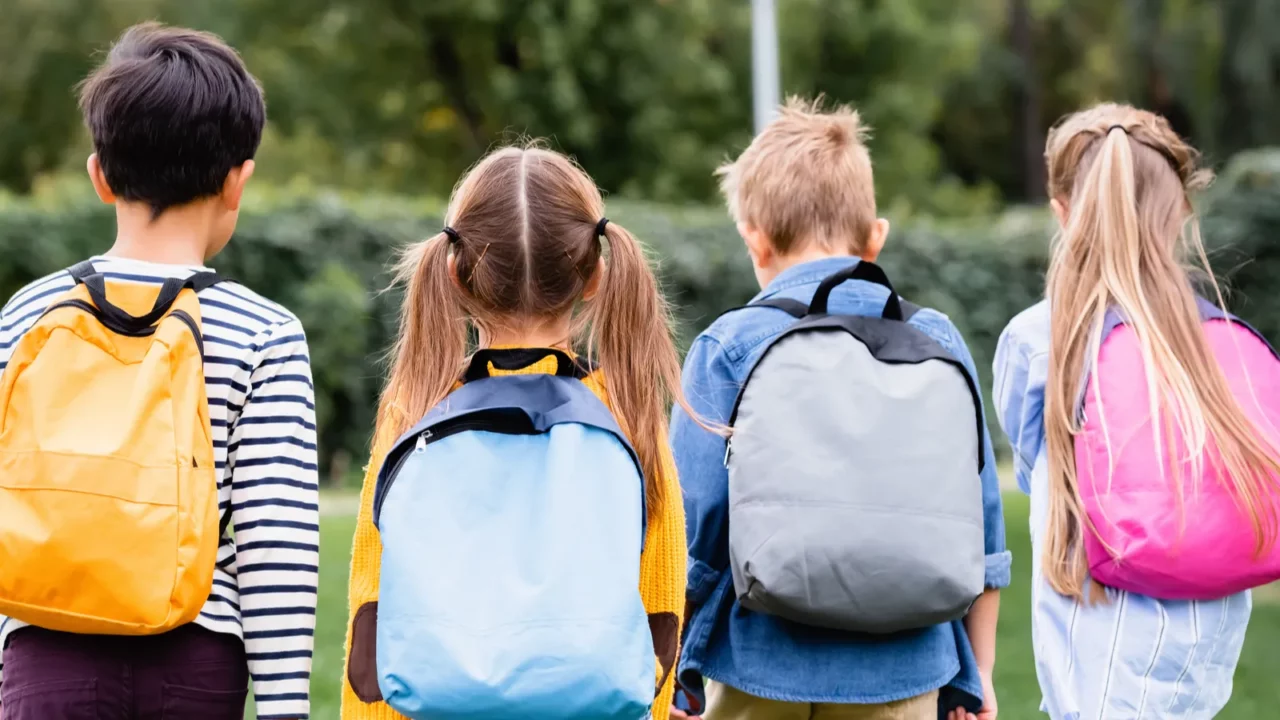 back view of schoolkids with backpacks walking on lawn