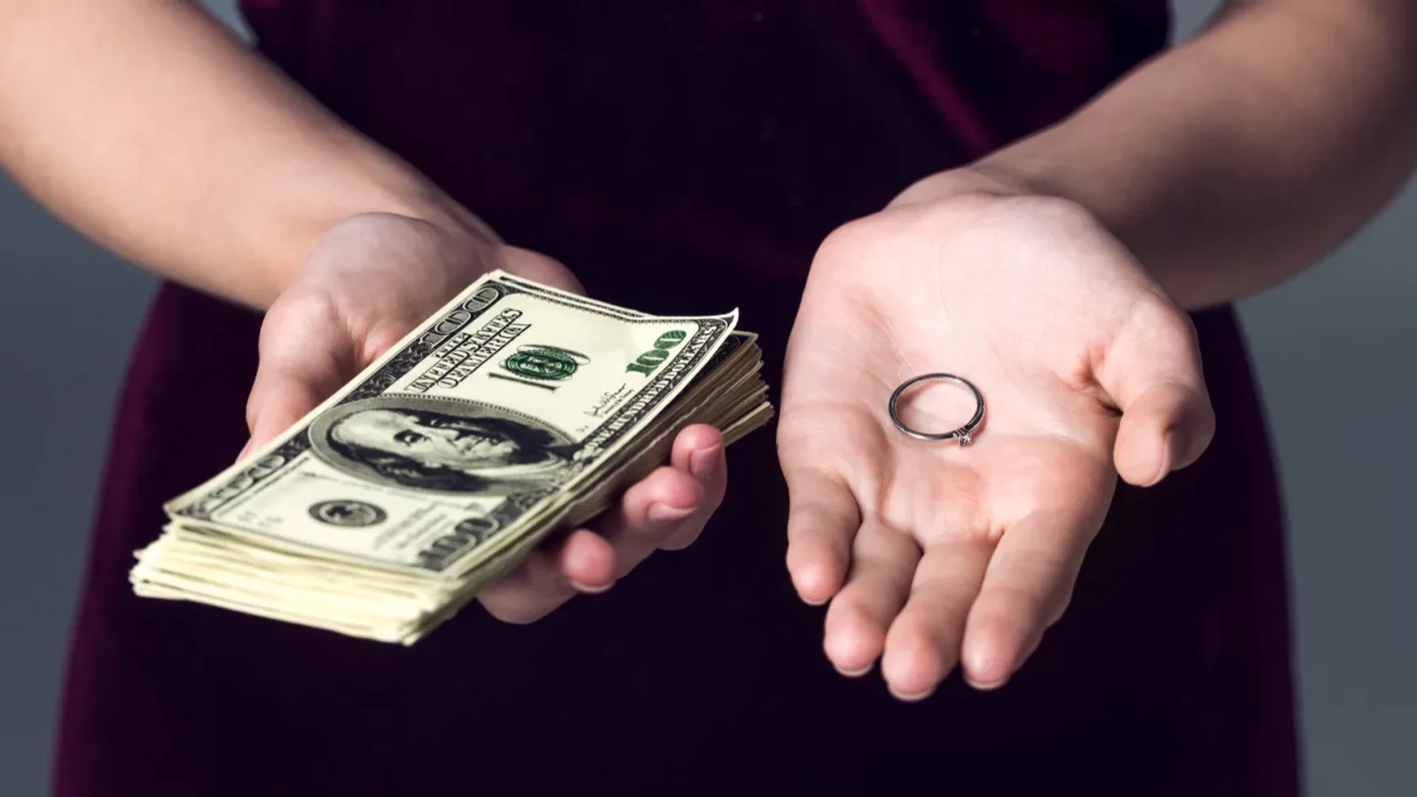 Cropped shot of woman holding stack of cash and wedding ring